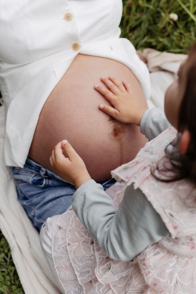 Kinderhand liegt sanft auf dem Babybauch beim Babybauch Fotoshooting