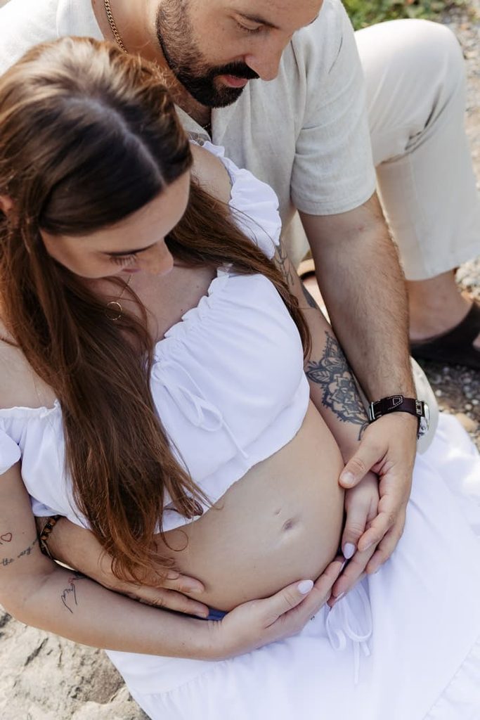 Werdende Eltern sitzen draussen, der Partner hält den Babybauch